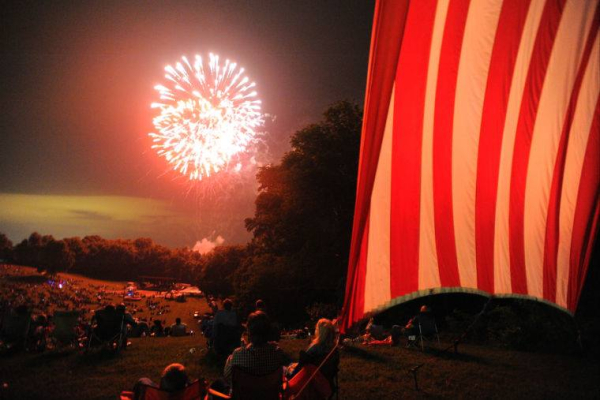 Spectators watch the fireworks light up the night sky at The Hayward Minton Thunderfest, framed by a massive American flag.