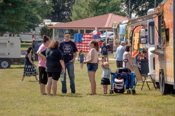 Festivalgoers chat near the food truck area as patriotic balloon décor fills the background.